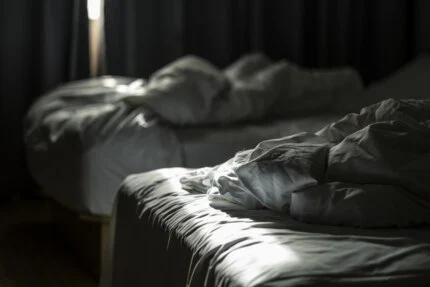 A beam of sunlight lands on the sheets of an unmade hotel bed