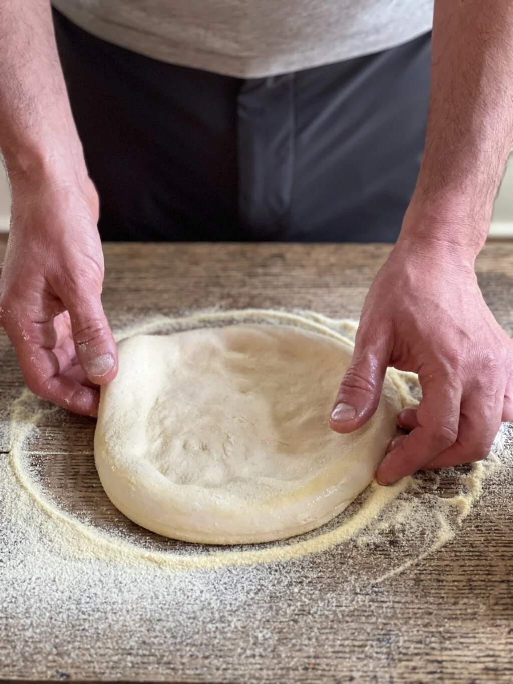 A rounded circle of pizza dough rests on a counter prior to being stretched
